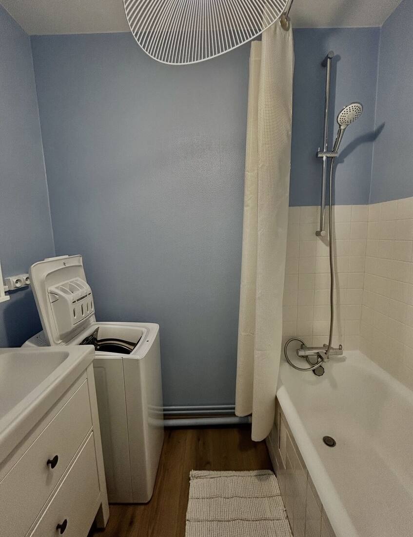 Salle de bain avec baignoire, colonne de douche, meuble vasque et lave-linge
